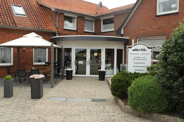 Neuloher Hof Backsteinbau mit weißer Eingangstür, großer Fensterfront, Sonnenschirm und Beschilderung des Neuloher Hofs.