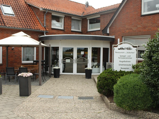 Neuloher Hof Backsteinbau mit weißer Eingangstür, großer Fensterfront, Sonnenschirm und Beschilderung des Neuloher Hofs.