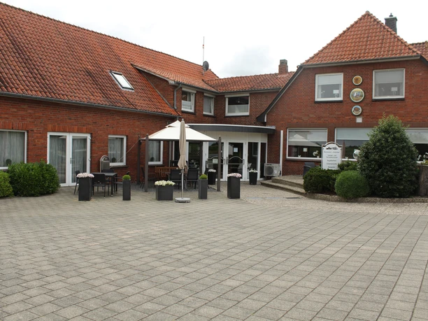 Brick-red restaurant with inviting terrace, parasols and planted flower pots in front.