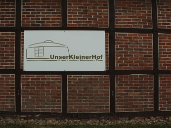 Unser kleiner Hof Ein Schild an einer Backsteinwand mit der Aufschrift "Unser Kleiner Hof - Urlaub - Jurten - Abenteuer - Tiere".A sign on a brick wall with the inscription "Our small farm - vacation - yurts - adventure - animals".Et skilt på en murstensvæg med påskriften "Our small farm - holiday - yurts - adventure - animals".Een bord op een bakstenen muur met de inscriptie "Onze kleine boerderij - vakantie - yurts - avontuur - dieren".