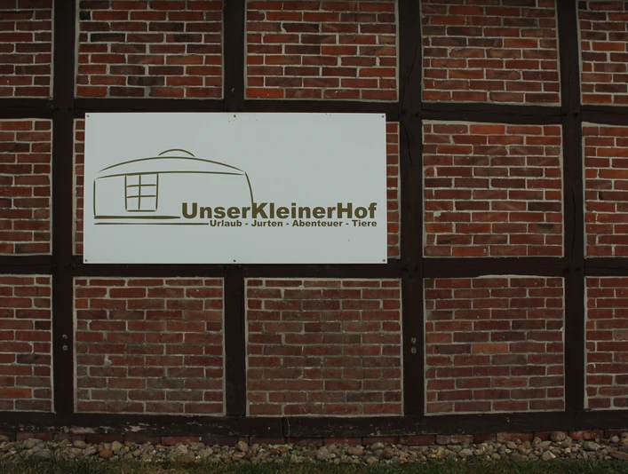 Unser kleiner Hof Ein Schild an einer Backsteinwand mit der Aufschrift "Unser Kleiner Hof - Urlaub - Jurten - Abenteuer - Tiere".A sign on a brick wall with the inscription "Our small farm - vacation - yurts - adventure - animals".Et skilt på en murstensvæg med påskriften "Our small farm - holiday - yurts - adventure - animals".Een bord op een bakstenen muur met de inscriptie "Onze kleine boerderij - vakantie - yurts - avontuur - dieren".