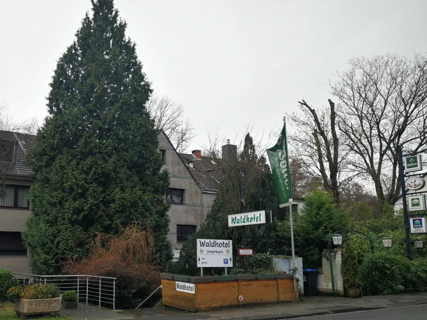 Waldhotel Unterbach nahe Erkrath Waldhotel Unterbach nahe Erkrath mit grüner Fassade, hohen Bäumen und einem einladenden Eingangsbereich.
