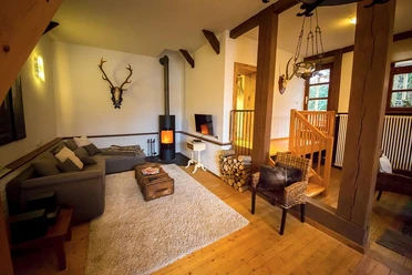 Wohnzimmer Forsthaus Gemütlicher Wohnraum mit Holzdekor, Kachelofen, Ecksofa, Teppich und rustikalem Ambiente.