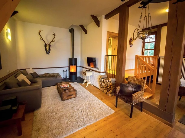 Wohnzimmer Forsthaus Gemütlicher Wohnraum mit Holzdekor, Kachelofen, Ecksofa, Teppich und rustikalem Ambiente.