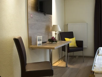 Zimmer Helles Hotelzimmer mit Holzfußboden, Flachbild-TV, Schreibtisch und moderner Sitzgelegenheit.