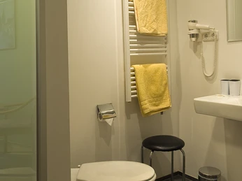 Badezimmer Barrierefreies Badezimmer mit wandmontierter Toilette, Handtuchheizkörper und Waschbecken mit Spiegel.