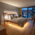 Modernes Doppelzimmer mit Holzfußboden, großem Bett, stilvoller Beleuchtung und Fenster mit Blick.
