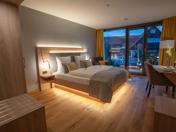 Modernes Doppelzimmer mit Holzfußboden, großem Bett, stilvoller Beleuchtung und Fenster mit Blick.