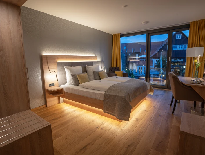 Modernes Doppelzimmer mit Holzfußboden, großem Bett, stilvoller Beleuchtung und Fenster mit Blick.
