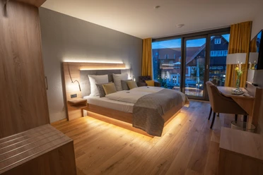 Doppelzimmer Modernes Doppelzimmer mit Holzfußboden, großem Bett, stilvoller Beleuchtung und Fenster mit Blick.