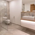 Modernes Badezimmer mit Dusche, Toilette, Waschbecken und minimalistischem Design in neutralen Tönen.