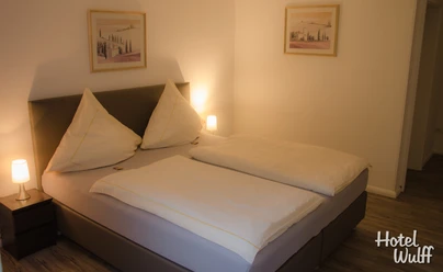 Doppelzimmer Ein einladendes Doppelzimmer mit zwei Nachttischen, Gemälden an den Wänden und stehendem Holzfußboden.