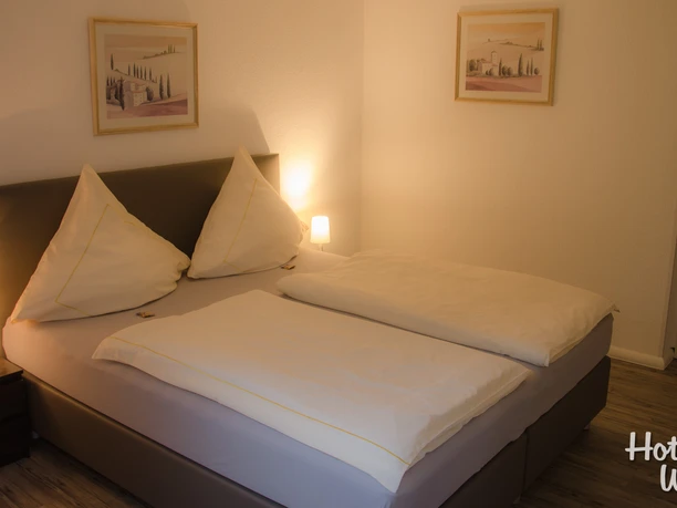 Doppelzimmer Ein einladendes Doppelzimmer mit zwei Nachttischen, Gemälden an den Wänden und stehendem Holzfußboden.