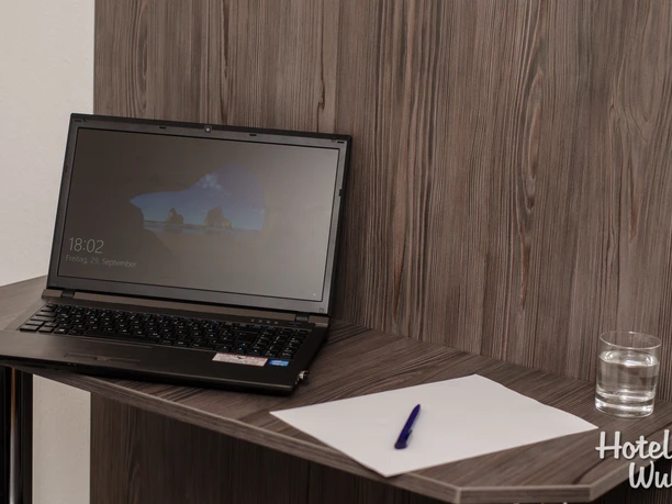 Schreibtisch Ein moderner Schreibtisch mit Laptop, Glas Wasser und einem Notizblatt mit Stift darauf.