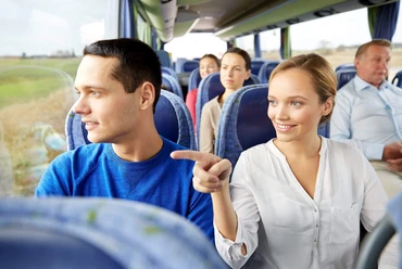 bustour-durch-die-parklandschaft.jpg Im Reisebus sitzen Menschen auf blauen Sitzen, lächelnd und aus dem Fenster schauend.
