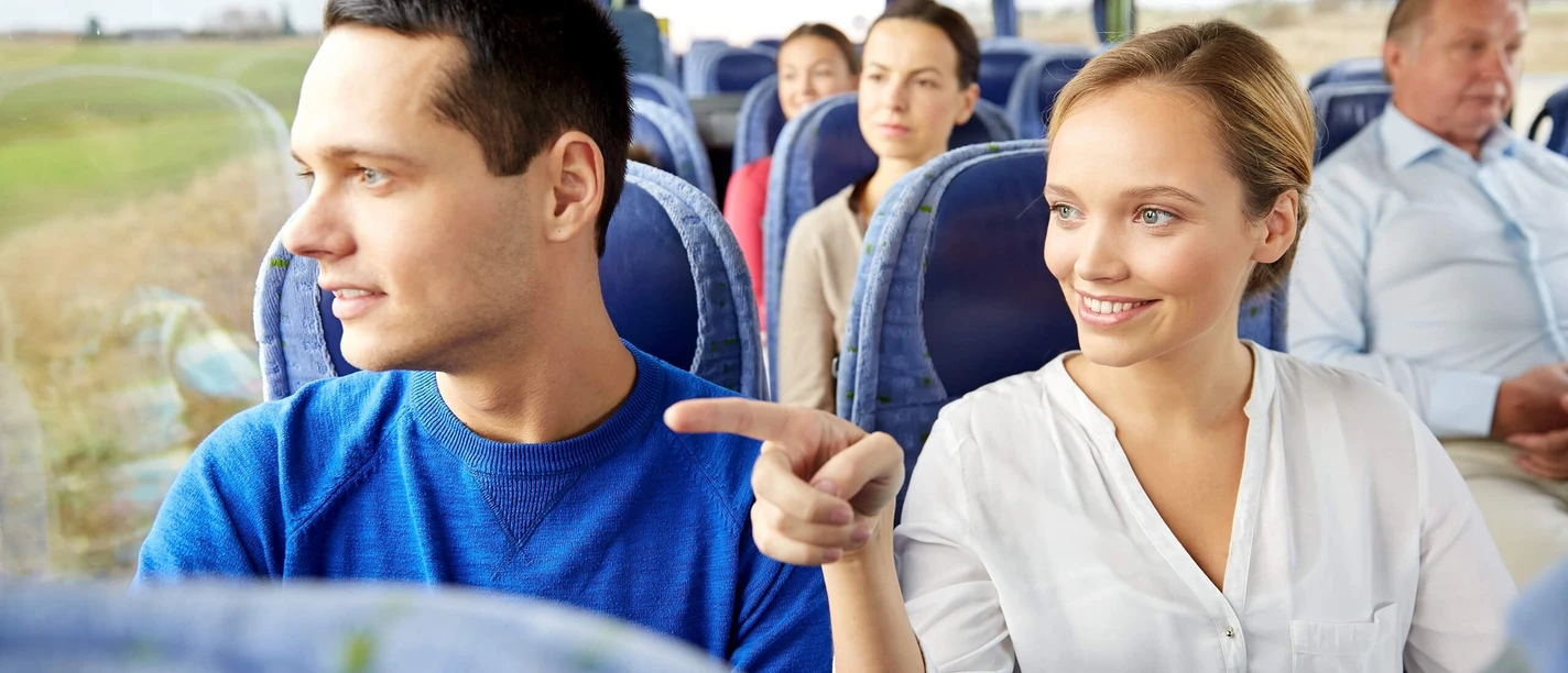 bustour-durch-die-parklandschaft.jpg Im Reisebus sitzen Menschen auf blauen Sitzen, lächelnd und aus dem Fenster schauend.