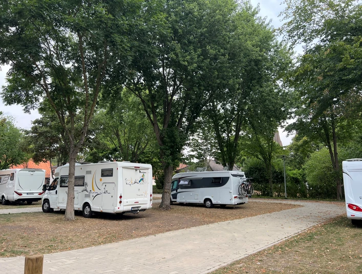 Wohnmobilstellplatz Bücken Wohnmobile stehen auf einem ruhigen Stellplatz unter hohen Bäumen, mit gepflasterten Wegen umgeben.