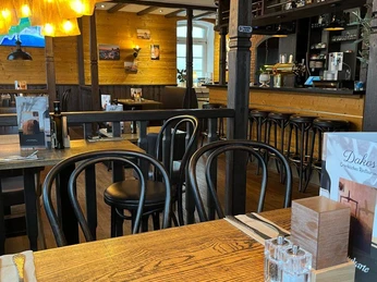 NieheimRestaurantDakos.jpg Ein gemütlicher Innenraum eines Restaurants mit Holzmöbeln und einem warmen Beleuchtungskonzept.