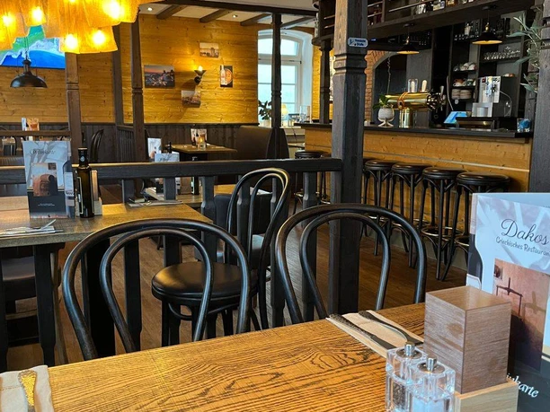 NieheimRestaurantDakos.jpg Ein gemütlicher Innenraum eines Restaurants mit Holzmöbeln und einem warmen Beleuchtungskonzept.