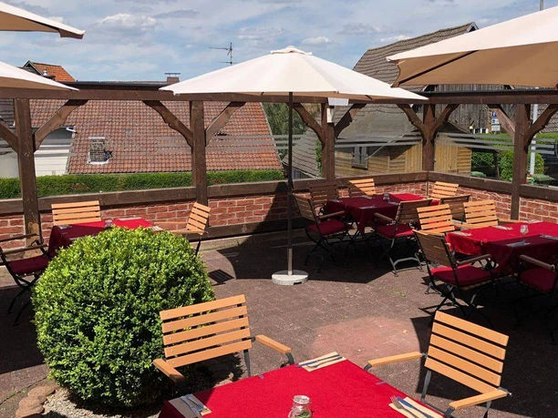 NieheimRestaurantDakos.jpg Sonning Terrasse eines Restaurants mit Holztischen und roten Tischdecken unter Sonnenschirmen.