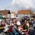 Lübbecke_Lübbecke tischt auf3_Silke_Birkemeyer.jpg Viele Menschen sitzen und stehen an Bierbänken auf einem belebten Marktplatz unter freiem Himmel.