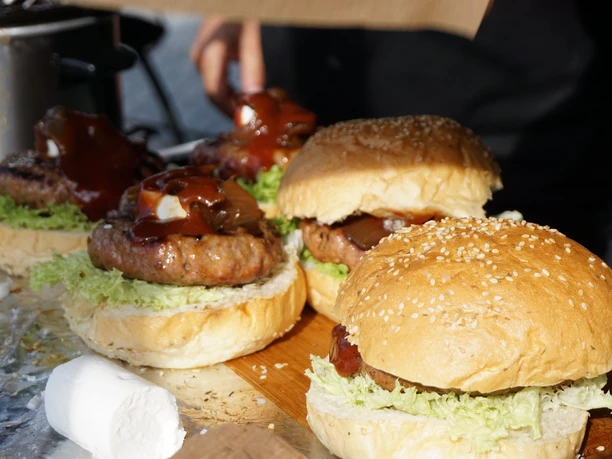 Lübbecke_Lübbecke tischt auf4_Silke_Birkemeyer.jpg Vier saftige Burger mit Brötchen und Salat, großzügig mit Barbecuesoße und Zwiebeln garniert.