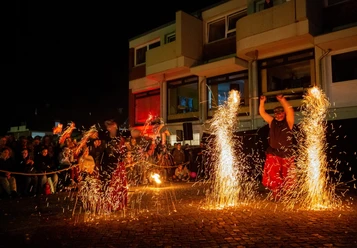 Feuerkünstler bei Nacht vor einem Publikum in einer städtischen Umgebung mit glühenden Funken.