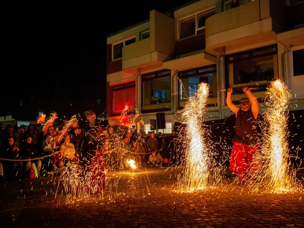 AdK Lübbecke Feuerkünstler bei Nacht vor einem Publikum in einer städtischen Umgebung mit glühenden Funken.