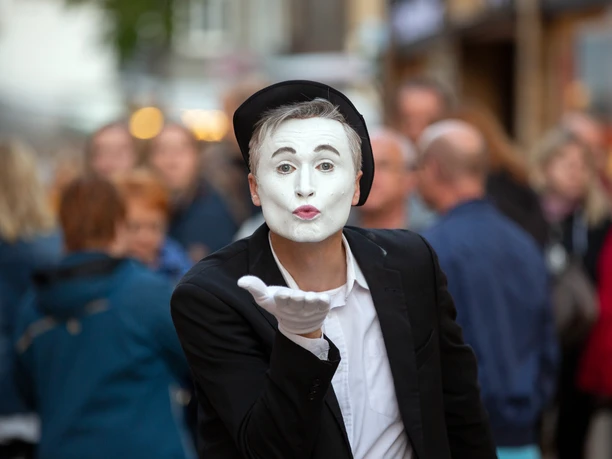 Lübbecke_Abend der Künste1_Oliver Krato.JPG Ein Pantomime-Künstler mit weiß geschminktem Gesicht schickt dem Publikum auf einer belebten Straße einen Kuss.