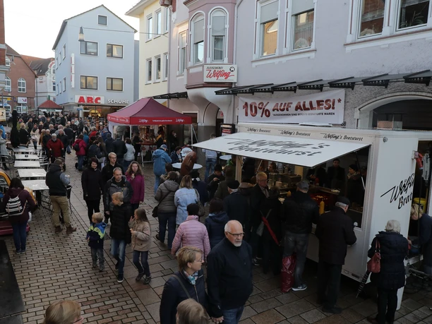 Menschen flanieren bei einem gut besuchten Straßenmarkt, umgeben von farbenfrohen Gebäuden.