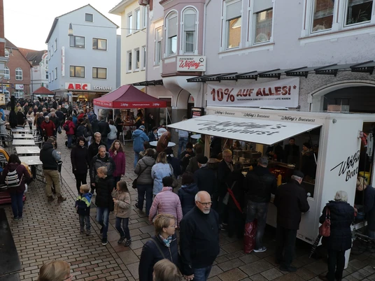 Lübbecke_Wurstmarkt2_Dennis Gilbert-Foto Pescht.jpg Menschen flanieren bei einem gut besuchten Straßenmarkt, umgeben von farbenfrohen Gebäuden.