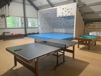 Innenraum der Kletterhalle mit Boulderwand, Tischtennisplatte, Billardtisch und hellen Fensterfronten.