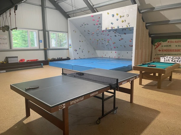 Innenraum der Kletterhalle mit Boulderwand, Tischtennisplatte, Billardtisch und hellen Fensterfronten.