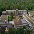 Titelbild Luftaufnahme eines großen, umgeben von Wald liegenden Gebäudekomplexes mit begrünten Flachdächern.