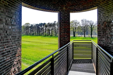 Landschaftsfenster Wemkendorf.JPG Blick durch einen Ziegelbogen auf grüne Wiesen und Bäume. Holzgeländer im Vordergrund.