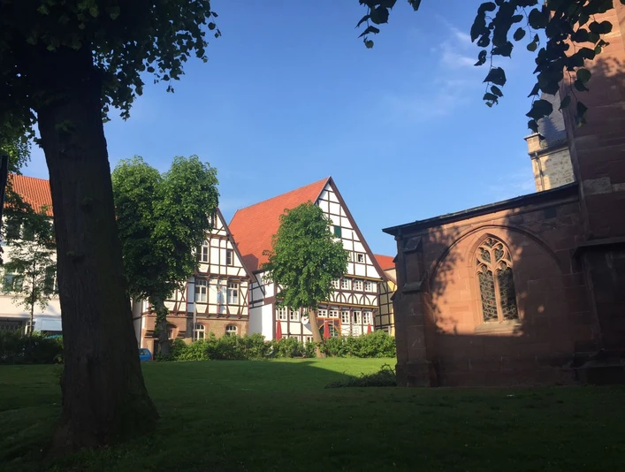 Hotel Alt Warburg Fachwerkfassade eines historischen Gebäudes in Warburg, umgeben von Bäumen und grüner Wiese.