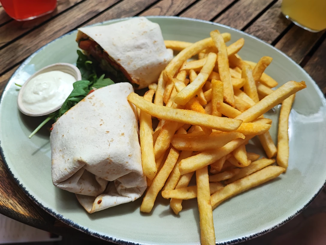 Wrap mit Pommes Ein Teller mit einem gefüllten Wrap, knusprigen Pommes und einem kleinen Becher mit weißer Soße.