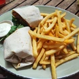 Wrap mit Pommes Ein Teller mit einem gefüllten Wrap, knusprigen Pommes und einem kleinen Becher mit weißer Soße.