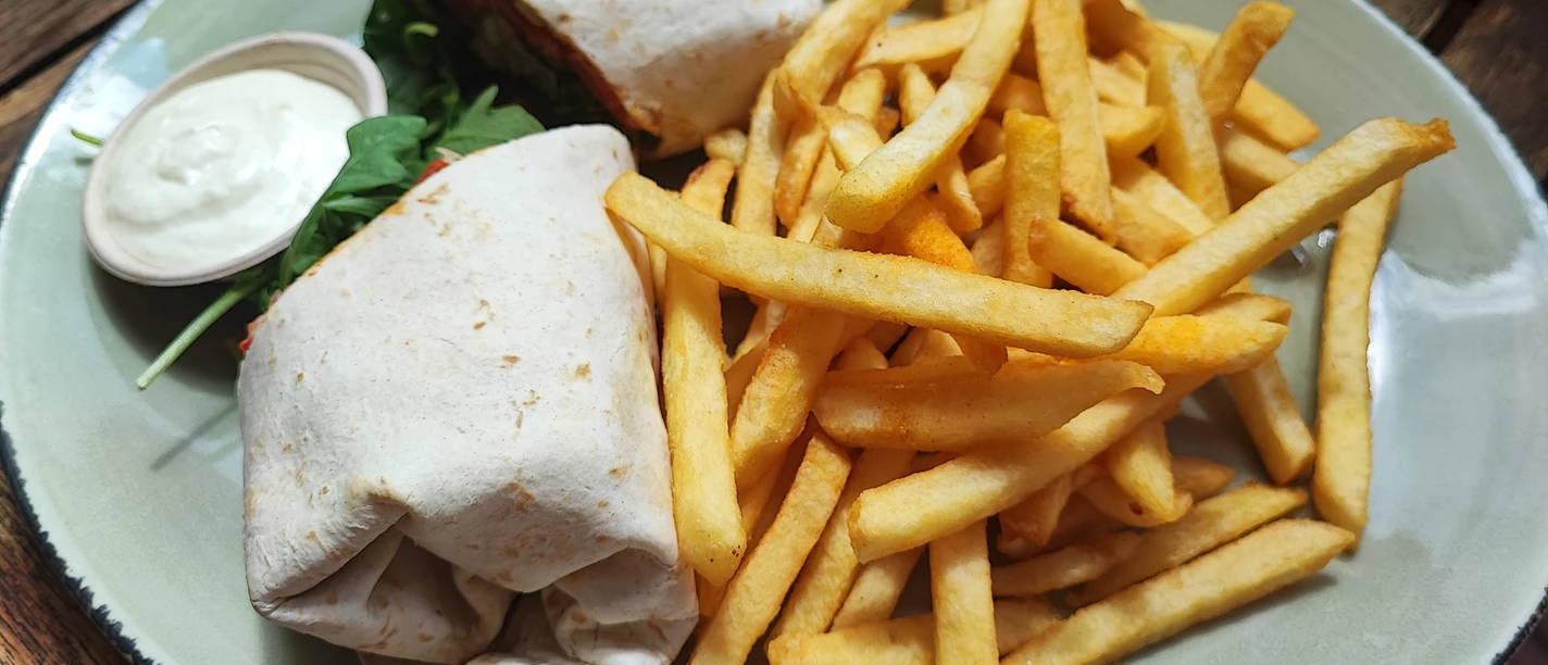 Wrap mit Pommes Ein Teller mit einem gefüllten Wrap, knusprigen Pommes und einem kleinen Becher mit weißer Soße.