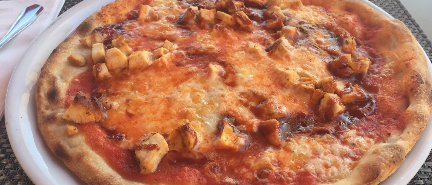 Pizza on a white plate, topped with juicy pieces of chicken and melted cheese.