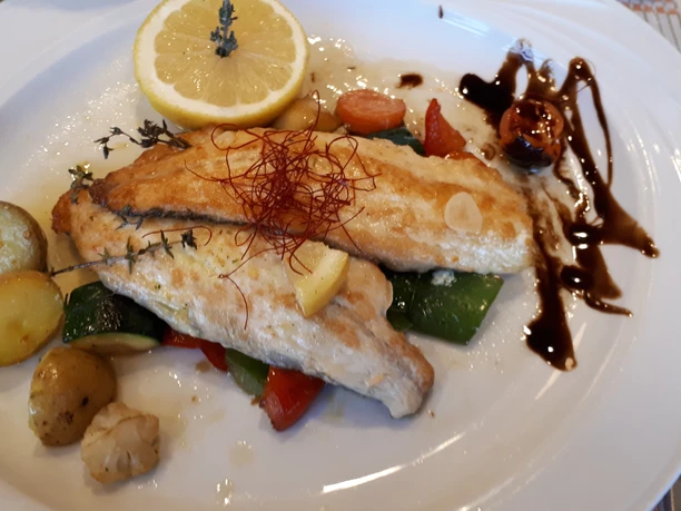 Fischteller Ein kunstvoll angerichteter Fischteller mit gebratenem Fischfilet, Gemüse, Zitrone und einer Balsamicoglasur.