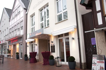 Blick von außen.jpg Ein italienisches Restaurant mit stilvoller Fassade, Markise und Stehtischen in einer Fußgängerzone.