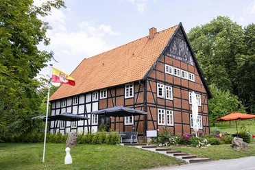appartmenthotel von außen.jpg Hotel mit rotem Ziegeldach und Fachwerk, umgeben von grünen Bäumen und mit sonniger Terrasse.