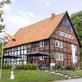 appartmenthotel von außen.jpg Hotel mit rotem Ziegeldach und Fachwerk, umgeben von grünen Bäumen und mit sonniger Terrasse.