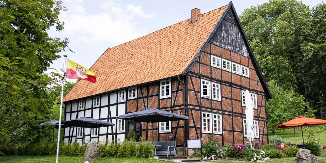 appartmenthotel von außen.jpg Hotel mit rotem Ziegeldach und Fachwerk, umgeben von grünen Bäumen und mit sonniger Terrasse.