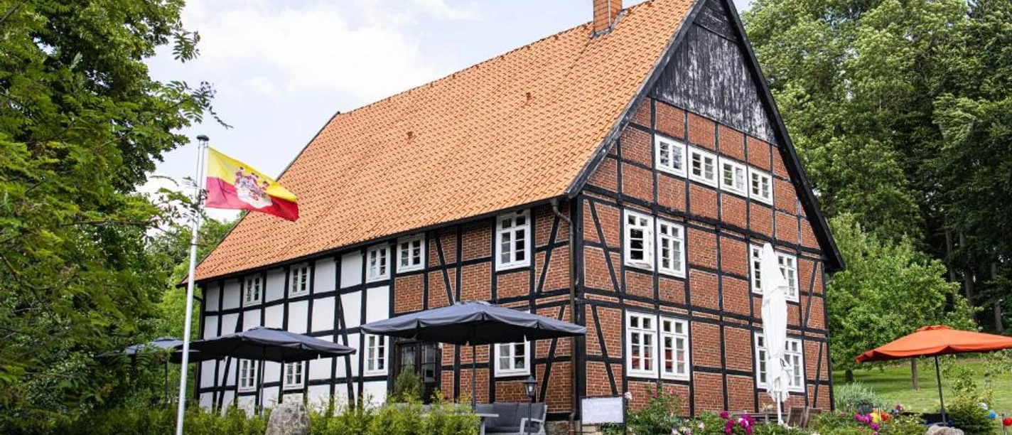 appartmenthotel von außen.jpg Hotel mit rotem Ziegeldach und Fachwerk, umgeben von grünen Bäumen und mit sonniger Terrasse.
