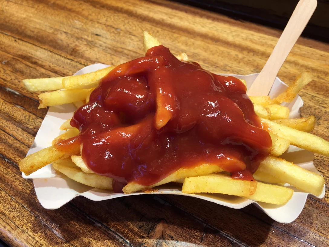 Pommes Pommes mit einer großzügigen Portion Ketchup auf einem weißen Pappteller, fotografiert auf einer Holzoberfläche.French fries with a generous portion of ketchup on a white paper plate, photographed on a wooden surface.Pommes frites med en generøs portion ketchup på en hvid paptallerken, fotograferet på et træunderlag.Friet met een flinke portie ketchup op een wit papieren bord, gefotografeerd op een houten ondergrond.