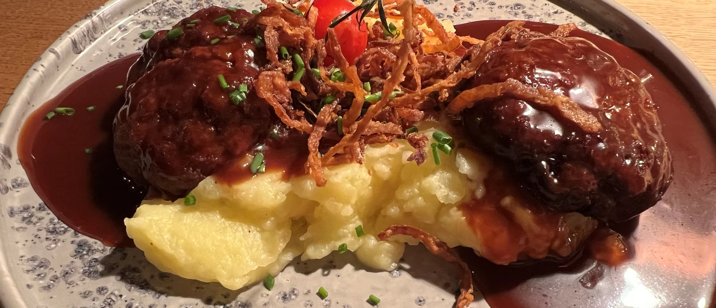 Frikadellen Hausgemachte Frikadellen auf einer Kartoffelbreimahlzeit, garniert mit Röstzwiebeln und Tomate.