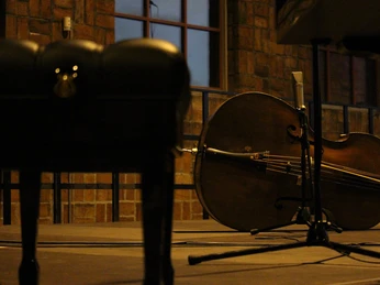 Violoncello Ein Violoncello liegt in einem gedämpft beleuchteten Raum auf einer Bühne vor einer Steinwand.