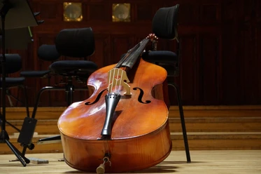 Kontrabass Ein Kontrabass lehnt auf einem hölzernen Konzertboden, umgeben von leeren Musiksesseln.